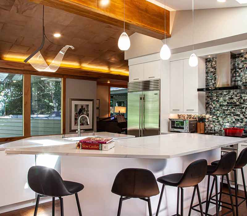 This kitchen remodel celebrates family, nature, and the unique geometry of the original home. It features crisp white cabinetry, cool-toned quartz countertops, two islands, and bold blue accents, plus a tactile mix of materials—wood, metal, glass, and stone—selected to stand the test of time in both durability and style.