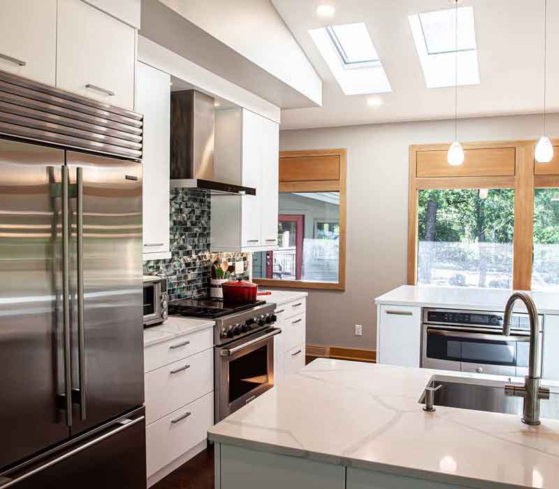 This kitchen remodel celebrates family, nature, and the unique geometry of the original home. It features crisp white cabinetry, cool-toned quartz countertops, two islands, and bold blue accents, plus a tactile mix of materials—wood, metal, glass, and stone—selected to stand the test of time in both durability and style.