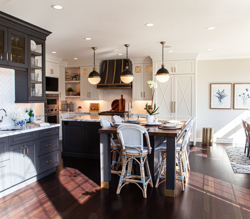 This light-filled, European inspired kitchen includes a bay windowed breakfast nook and opens onto an expansive deck. The striking black cabinetry coordinates with the black and brass pendant lamps and range hood.