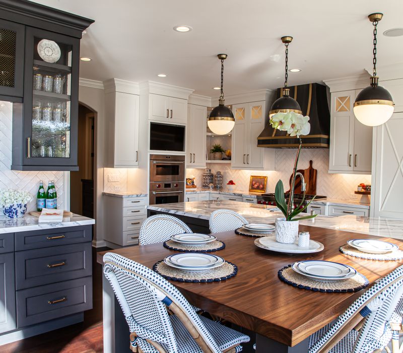 This light-filled, European inspired kitchen includes a bay windowed breakfast nook and opens onto an expansive deck. The striking black cabinetry coordinates with the black and brass pendant lamps and range hood.