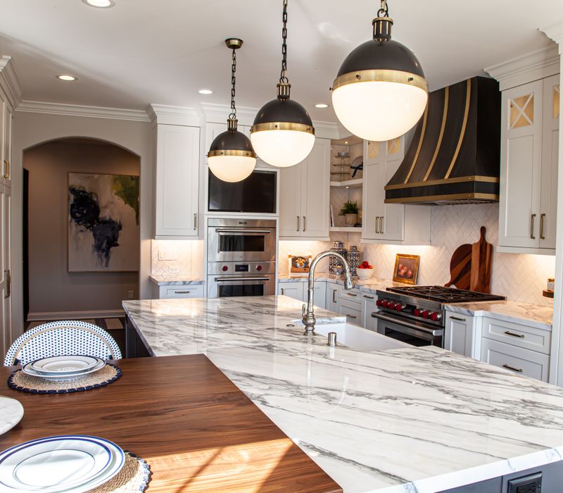 This light-filled, European inspired kitchen includes a bay windowed breakfast nook and opens onto an expansive deck. The striking black cabinetry coordinates with the black and brass pendant lamps and range hood.