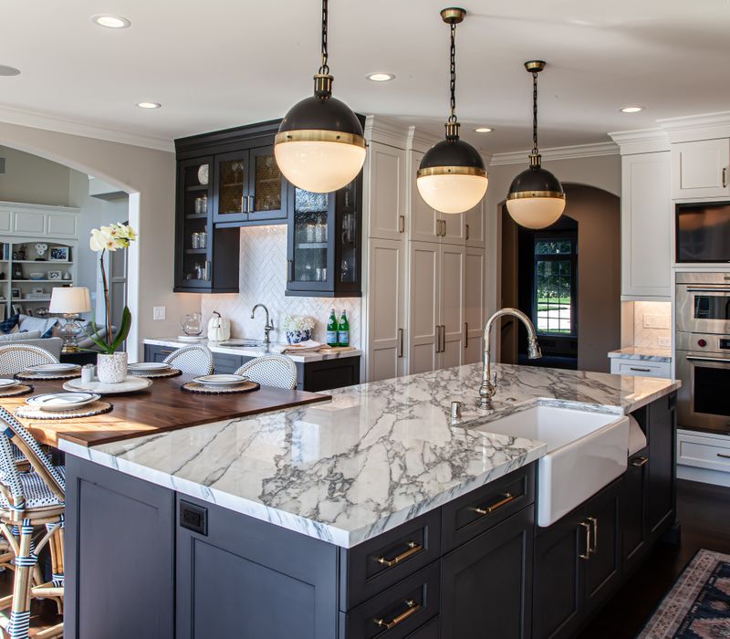 This light-filled, European inspired kitchen includes a bay windowed breakfast nook and opens onto an expansive deck. The striking black cabinetry coordinates with the black and brass pendant lamps and range hood.