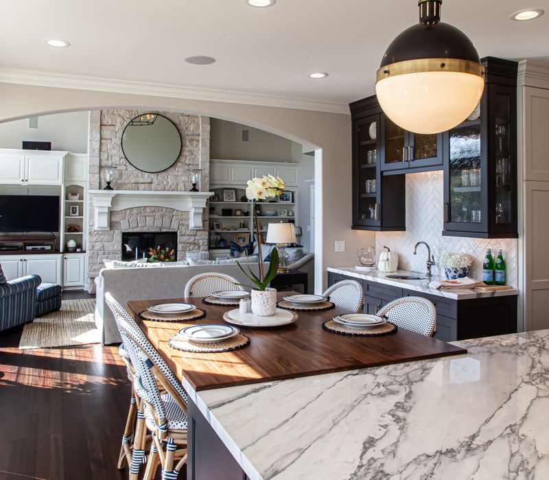 This light-filled, European inspired kitchen includes a bay windowed breakfast nook and opens onto an expansive deck. The striking black cabinetry coordinates with the black and brass pendant lamps and range hood.