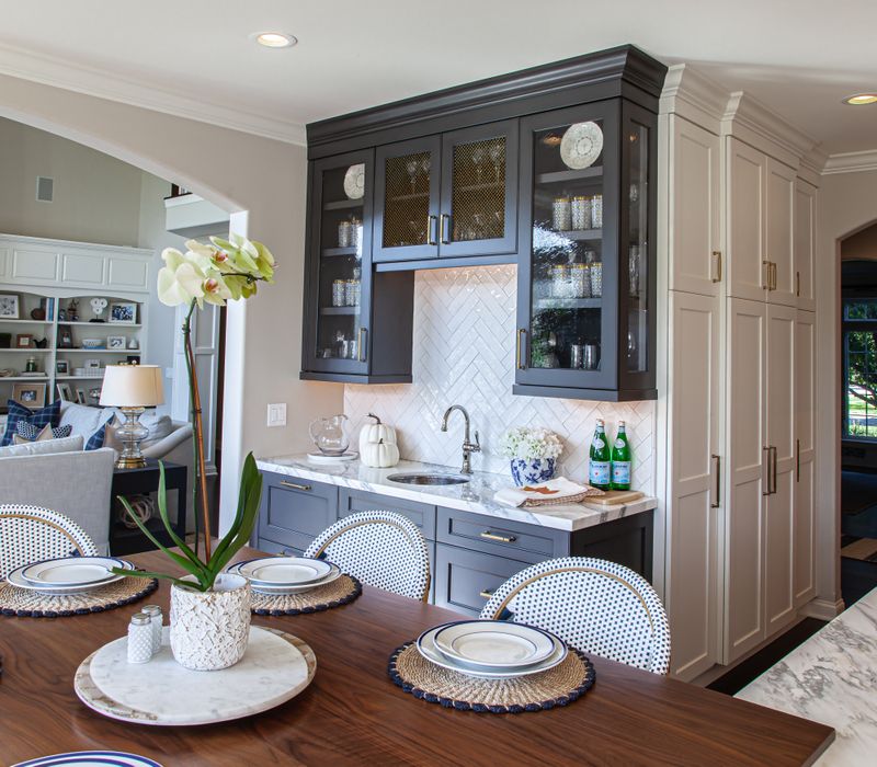 This light-filled, European inspired kitchen includes a bay windowed breakfast nook and opens onto an expansive deck. The striking black cabinetry coordinates with the black and brass pendant lamps and range hood.