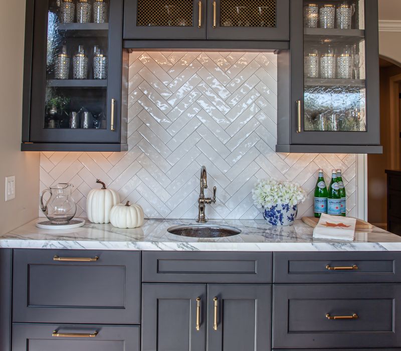 This light-filled, European inspired kitchen includes a bay windowed breakfast nook and opens onto an expansive deck. The striking black cabinetry coordinates with the black and brass pendant lamps and range hood.