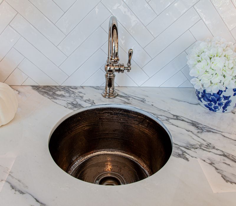 This light-filled, European inspired kitchen includes a bay windowed breakfast nook and opens onto an expansive deck. The striking black cabinetry coordinates with the black and brass pendant lamps and range hood.