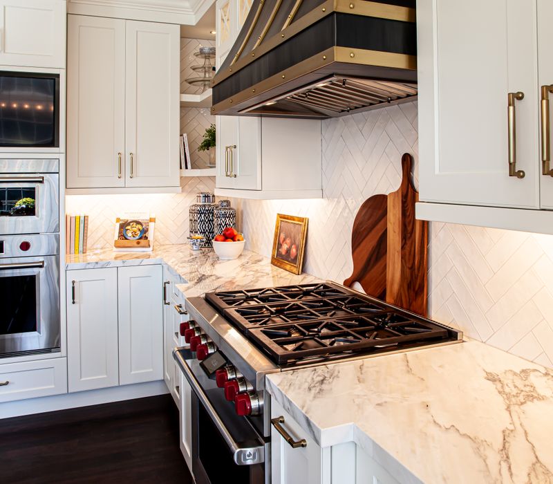 This light-filled, European inspired kitchen includes a bay windowed breakfast nook and opens onto an expansive deck. The striking black cabinetry coordinates with the black and brass pendant lamps and range hood.