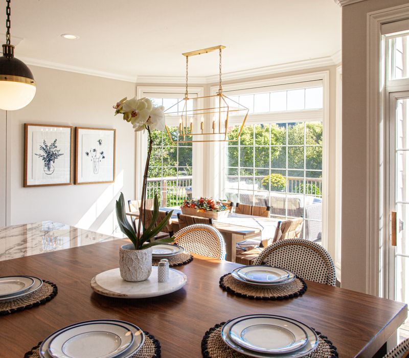 This light-filled, European inspired kitchen includes a bay windowed breakfast nook and opens onto an expansive deck. The striking black cabinetry coordinates with the black and brass pendant lamps and range hood.