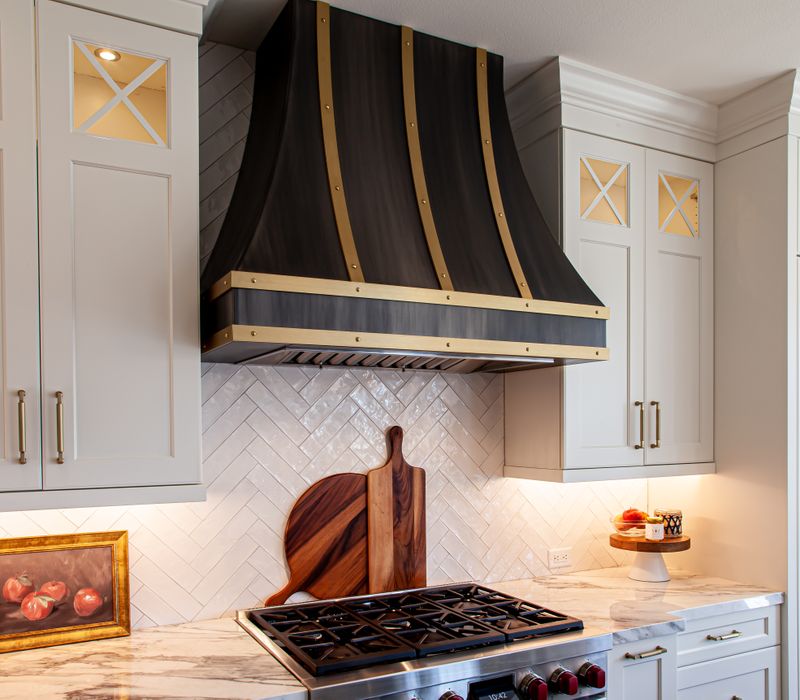 This light-filled, European inspired kitchen includes a bay windowed breakfast nook and opens onto an expansive deck. The striking black cabinetry coordinates with the black and brass pendant lamps and range hood.