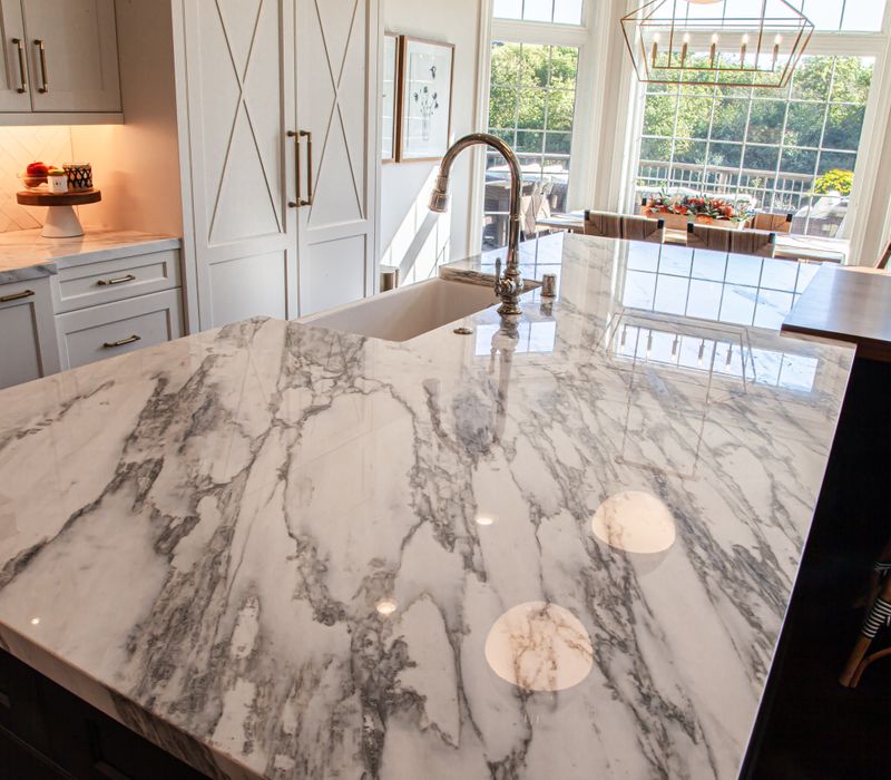 This light-filled, European inspired kitchen includes a bay windowed breakfast nook and opens onto an expansive deck. The striking black cabinetry coordinates with the black and brass pendant lamps and range hood.