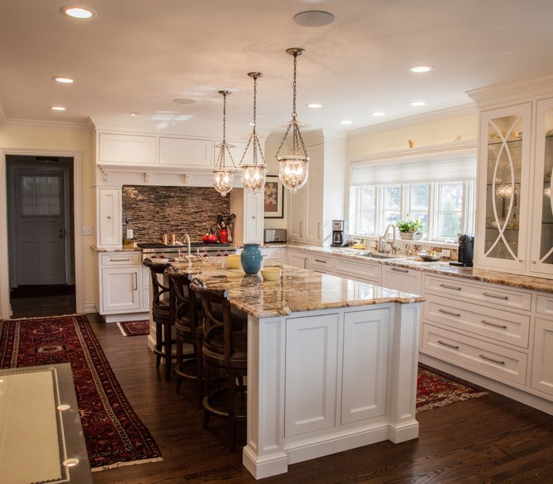 Hardwood floors, polished stone countertops, a mosaic stone tile backsplash, white glass-front cabinetry, and glass pendant lanterns combine in this spacious kitchen.