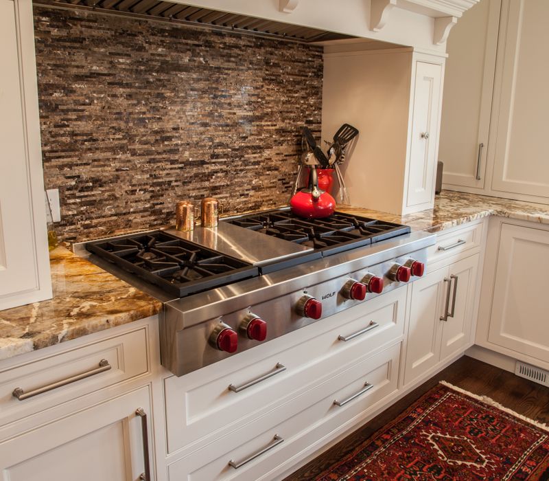 Hardwood floors, polished stone countertops, a mosaic stone tile backsplash, white glass-front cabinetry, and glass pendant lanterns combine in this spacious kitchen.