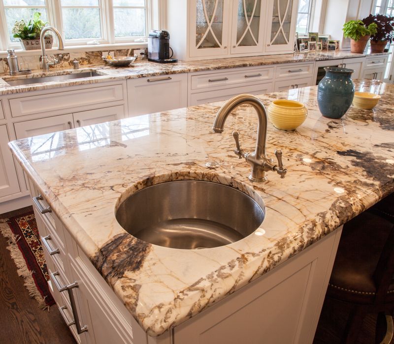 Hardwood floors, polished stone countertops, a mosaic stone tile backsplash, white glass-front cabinetry, and glass pendant lanterns combine in this spacious kitchen.