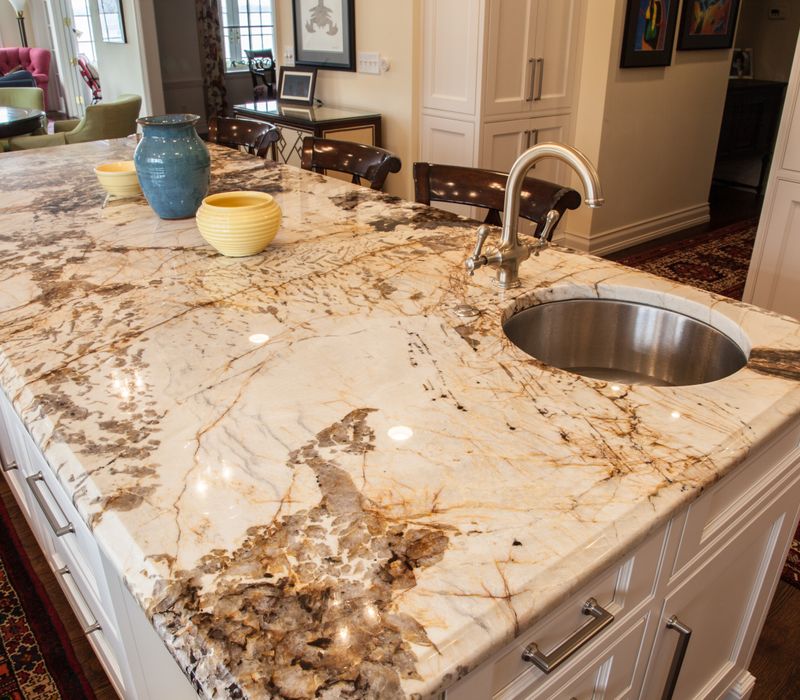 Hardwood floors, polished stone countertops, a mosaic stone tile backsplash, white glass-front cabinetry, and glass pendant lanterns combine in this spacious kitchen.