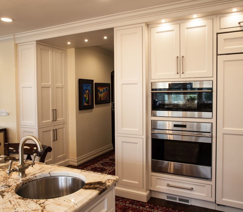 Hardwood floors, polished stone countertops, a mosaic stone tile backsplash, white glass-front cabinetry, and glass pendant lanterns combine in this spacious kitchen.