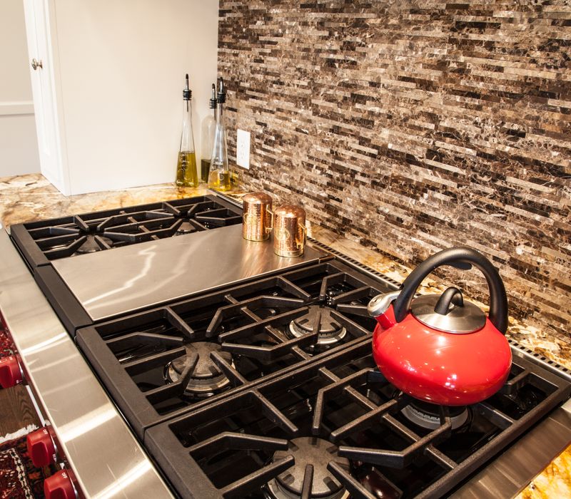 Hardwood floors, polished stone countertops, a mosaic stone tile backsplash, white glass-front cabinetry, and glass pendant lanterns combine in this spacious kitchen.