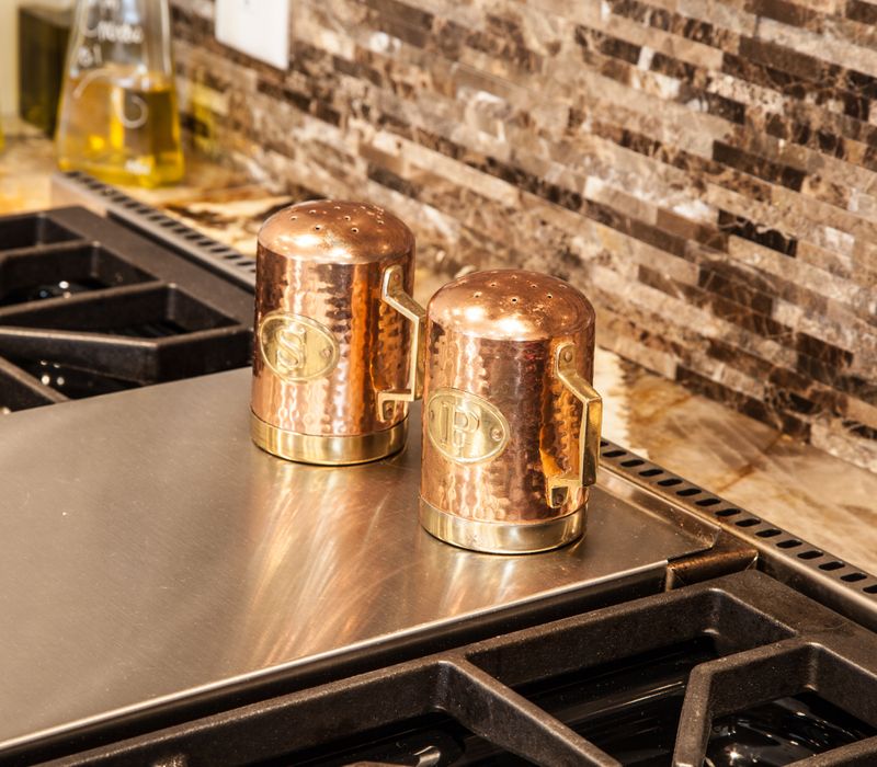 Hardwood floors, polished stone countertops, a mosaic stone tile backsplash, white glass-front cabinetry, and glass pendant lanterns combine in this spacious kitchen.