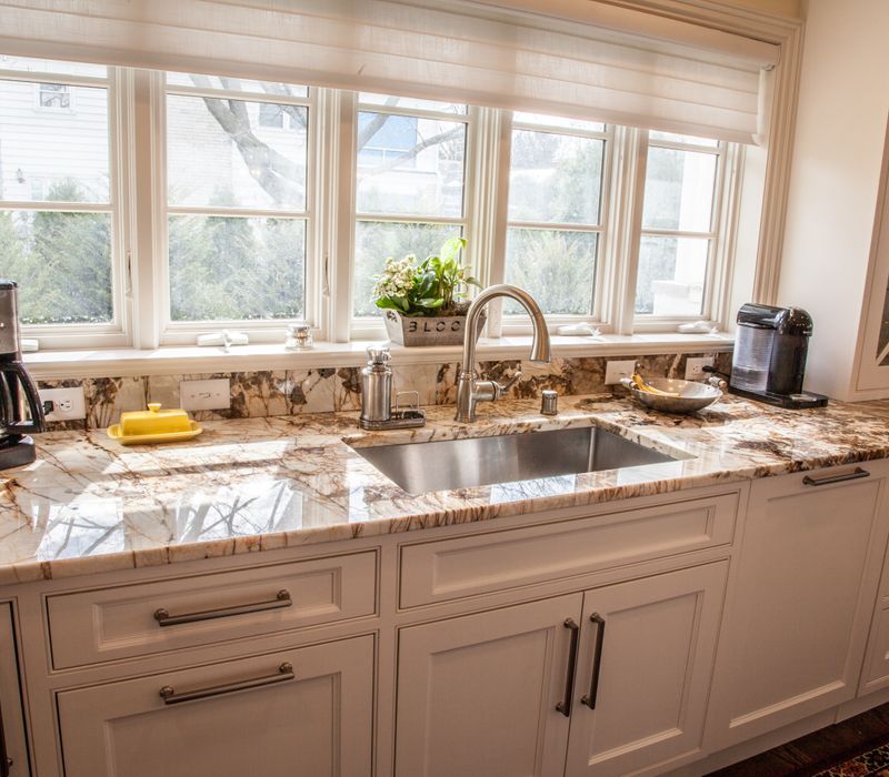Hardwood floors, polished stone countertops, a mosaic stone tile backsplash, white glass-front cabinetry, and glass pendant lanterns combine in this spacious kitchen.