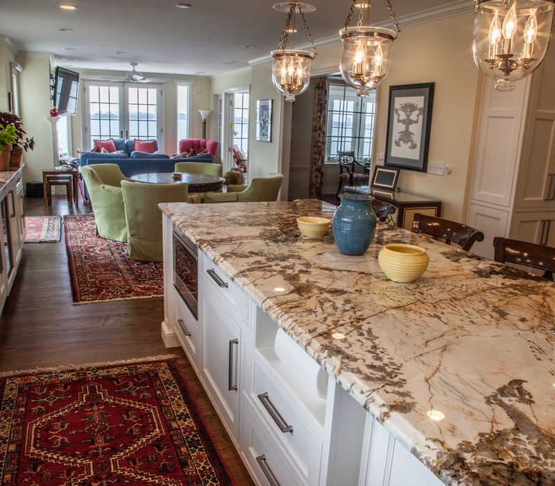 Hardwood floors, polished stone countertops, a mosaic stone tile backsplash, white glass-front cabinetry, and glass pendant lanterns combine in this spacious kitchen.