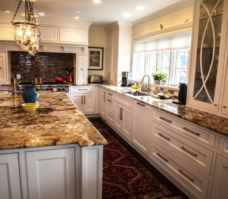 Hardwood floors, polished stone countertops, a mosaic stone tile backsplash, white glass-front cabinetry, and glass pendant lanterns combine in this spacious kitchen.