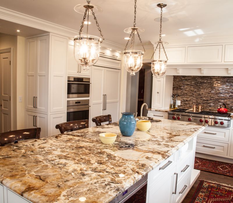 Hardwood floors, polished stone countertops, a mosaic stone tile backsplash, white glass-front cabinetry, and glass pendant lanterns combine in this spacious kitchen.