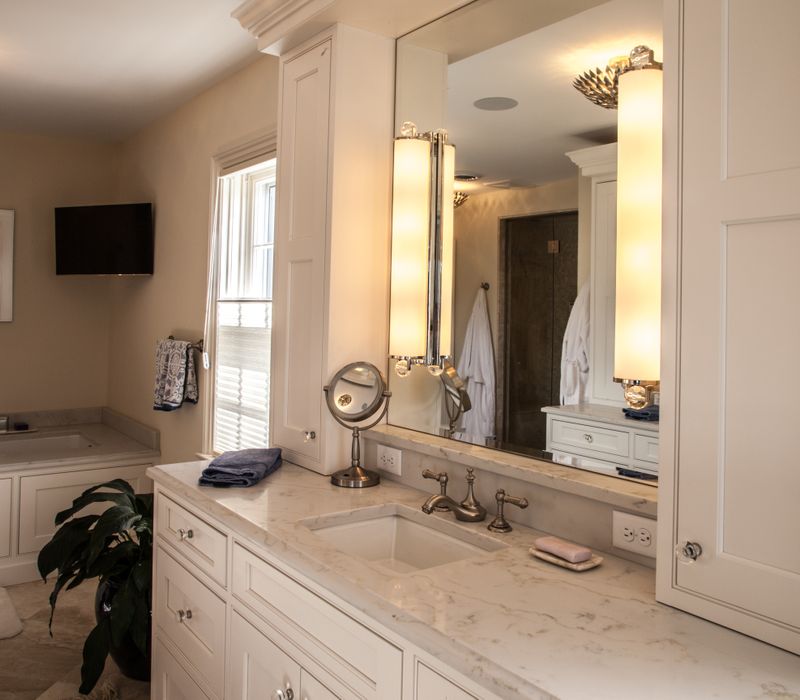 Hardwood floors, polished stone countertops, a mosaic stone tile backsplash, white glass-front cabinetry, and glass pendant lanterns combine in this spacious kitchen.