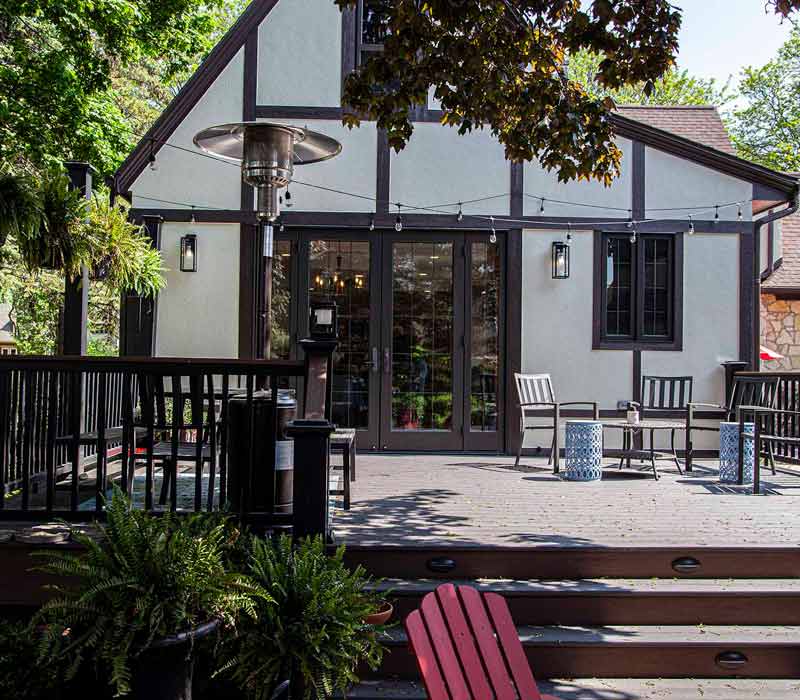 A kitchen featuring end-grain countertop, hardwood floors, and white glass tiles opens out onto a spacious deck in this Tudor style house.
