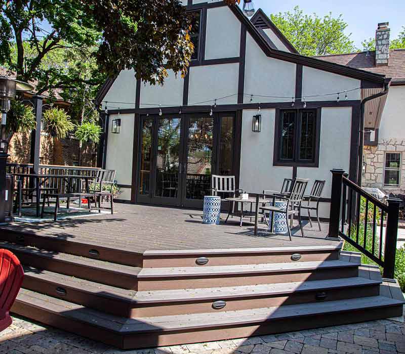 A kitchen featuring end-grain countertop, hardwood floors, and white glass tiles opens out onto a spacious deck in this Tudor style house.