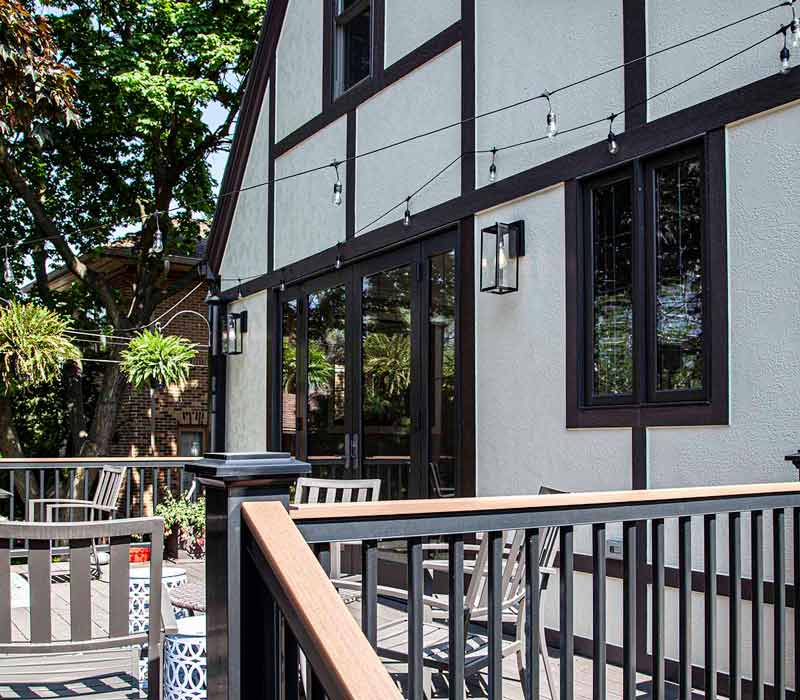 A kitchen featuring end-grain countertop, hardwood floors, and white glass tiles opens out onto a spacious deck in this Tudor style house.