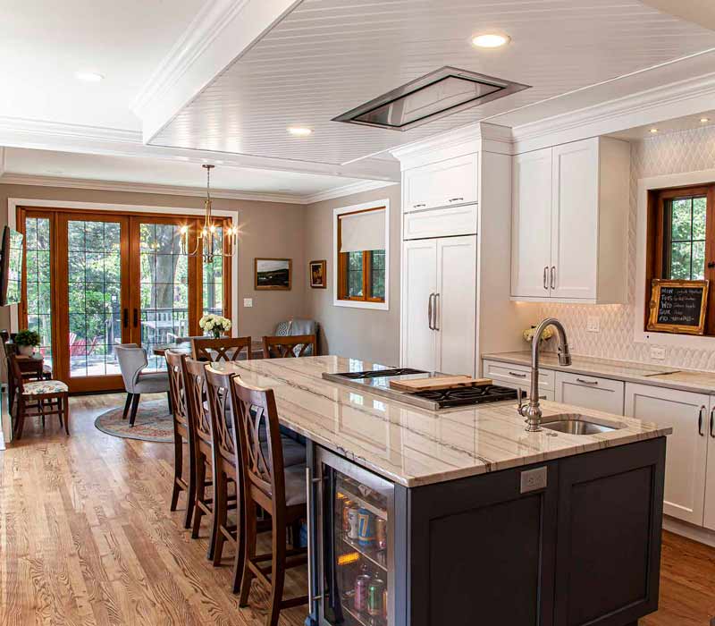 A kitchen featuring end-grain countertop, hardwood floors, and white glass tiles opens out onto a spacious deck in this Tudor style house.