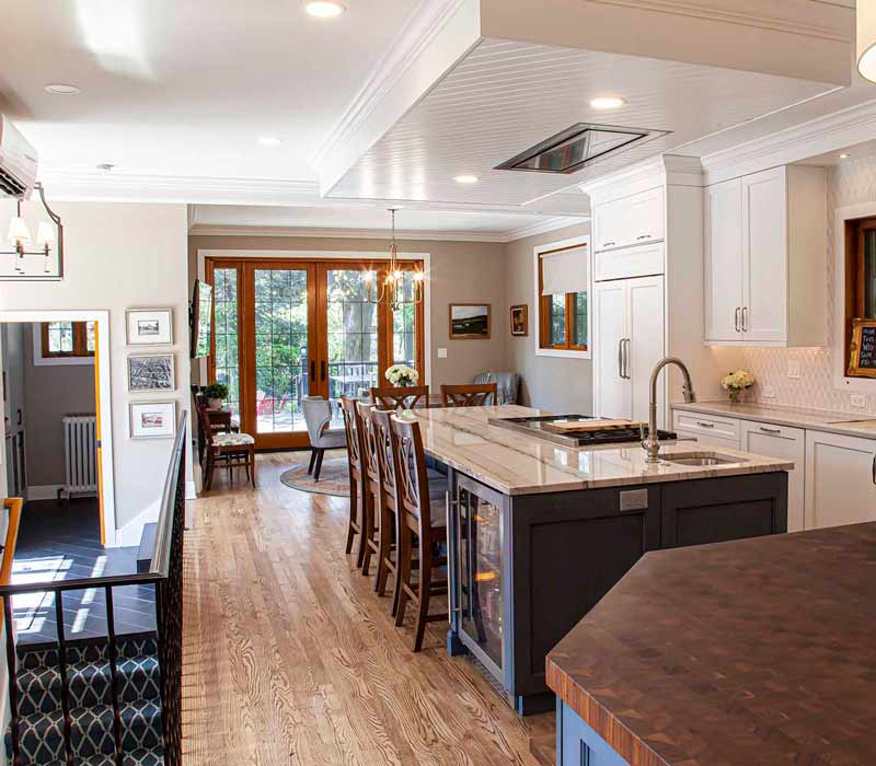 A kitchen featuring end-grain countertop, hardwood floors, and white glass tiles opens out onto a spacious deck in this Tudor style house.