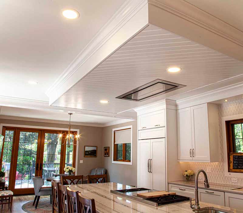 A kitchen featuring end-grain countertop, hardwood floors, and white glass tiles opens out onto a spacious deck in this Tudor style house.