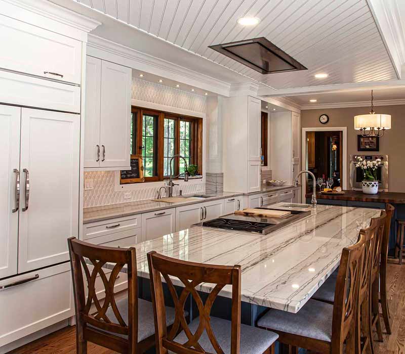 A kitchen featuring end-grain countertop, hardwood floors, and white glass tiles opens out onto a spacious deck in this Tudor style house.