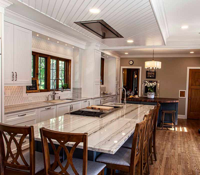 A kitchen featuring end-grain countertop, hardwood floors, and white glass tiles opens out onto a spacious deck in this Tudor style house.