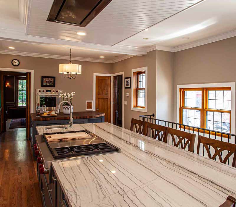 A kitchen featuring end-grain countertop, hardwood floors, and white glass tiles opens out onto a spacious deck in this Tudor style house.