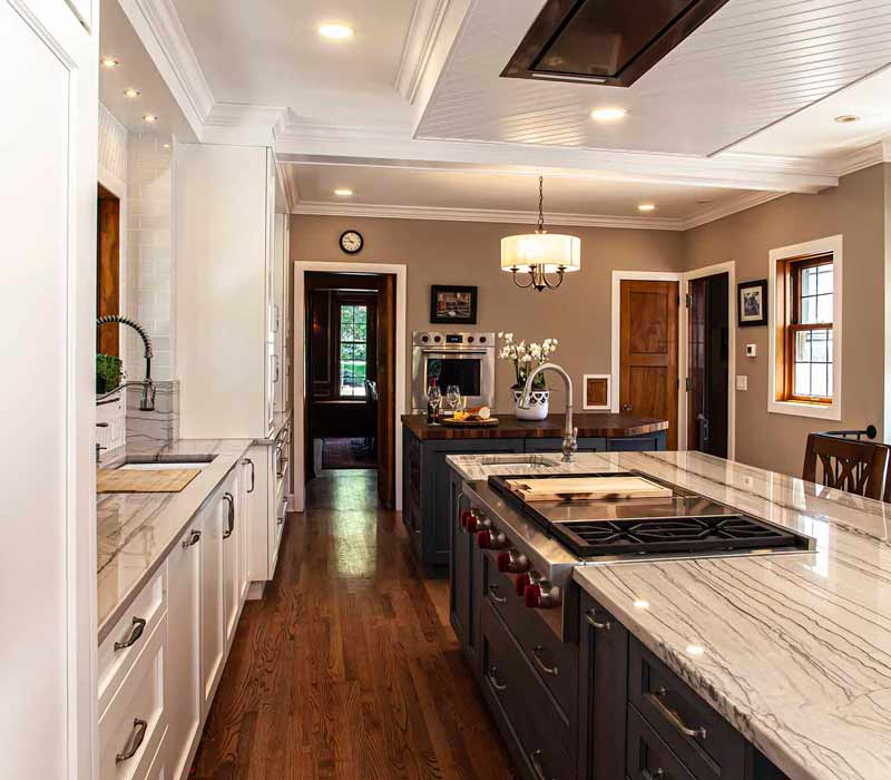 A kitchen featuring end-grain countertop, hardwood floors, and white glass tiles opens out onto a spacious deck in this Tudor style house.
