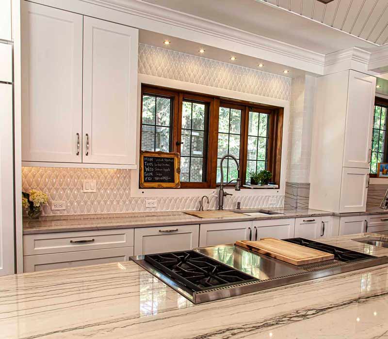 A kitchen featuring end-grain countertop, hardwood floors, and white glass tiles opens out onto a spacious deck in this Tudor style house.