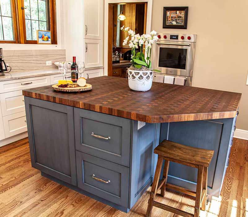 A kitchen featuring end-grain countertop, hardwood floors, and white glass tiles opens out onto a spacious deck in this Tudor style house.