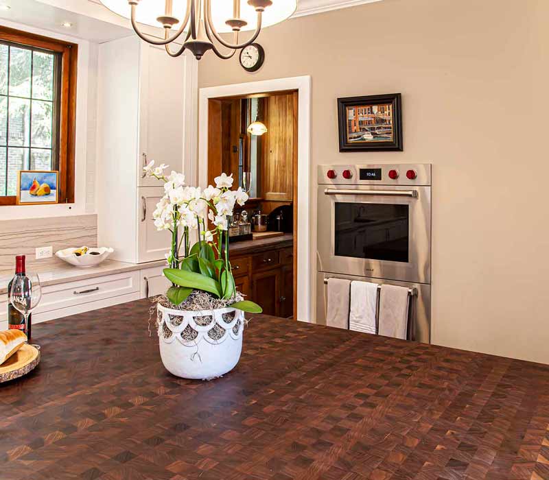 A kitchen featuring end-grain countertop, hardwood floors, and white glass tiles opens out onto a spacious deck in this Tudor style house.