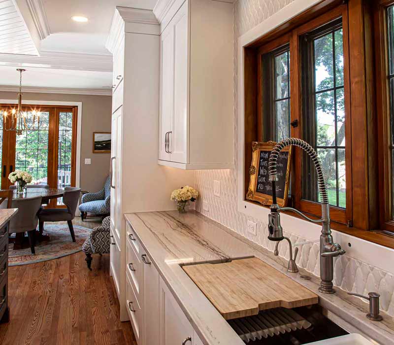 A kitchen featuring end-grain countertop, hardwood floors, and white glass tiles opens out onto a spacious deck in this Tudor style house.