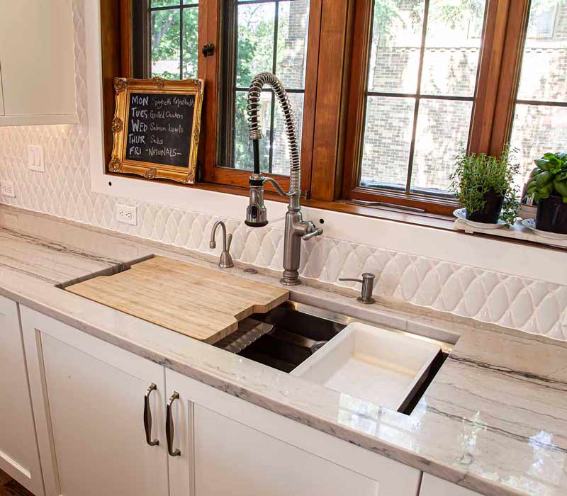 A kitchen featuring end-grain countertop, hardwood floors, and white glass tiles opens out onto a spacious deck in this Tudor style house.