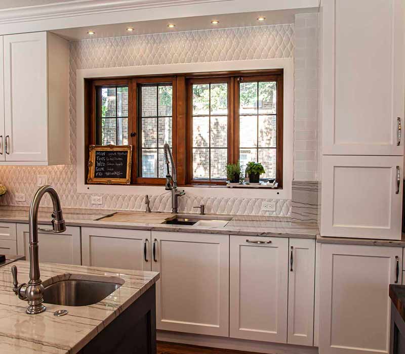 A kitchen featuring end-grain countertop, hardwood floors, and white glass tiles opens out onto a spacious deck in this Tudor style house.