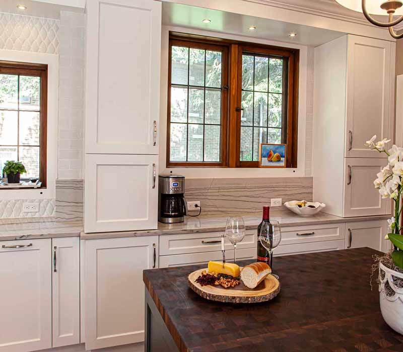 A kitchen featuring end-grain countertop, hardwood floors, and white glass tiles opens out onto a spacious deck in this Tudor style house.