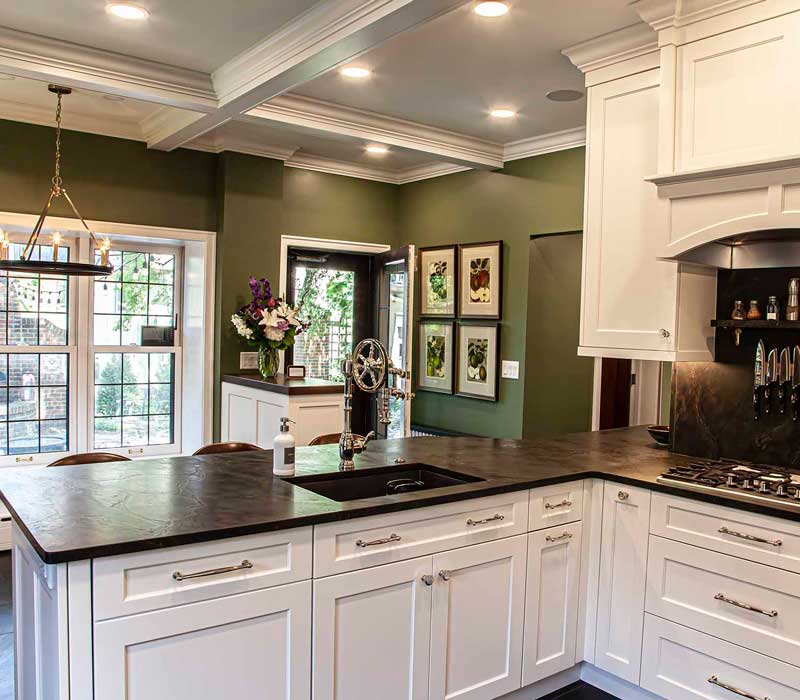 A chrome pull-down wheel faucet is the centerpiece of this traditional kitchen with natural slate countertops, art nouveau floral wallpaper, and green walls.