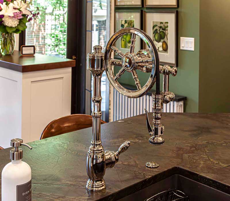 A chrome pull-down wheel faucet is the centerpiece of this traditional kitchen with natural slate countertops, art nouveau floral wallpaper, and green walls.