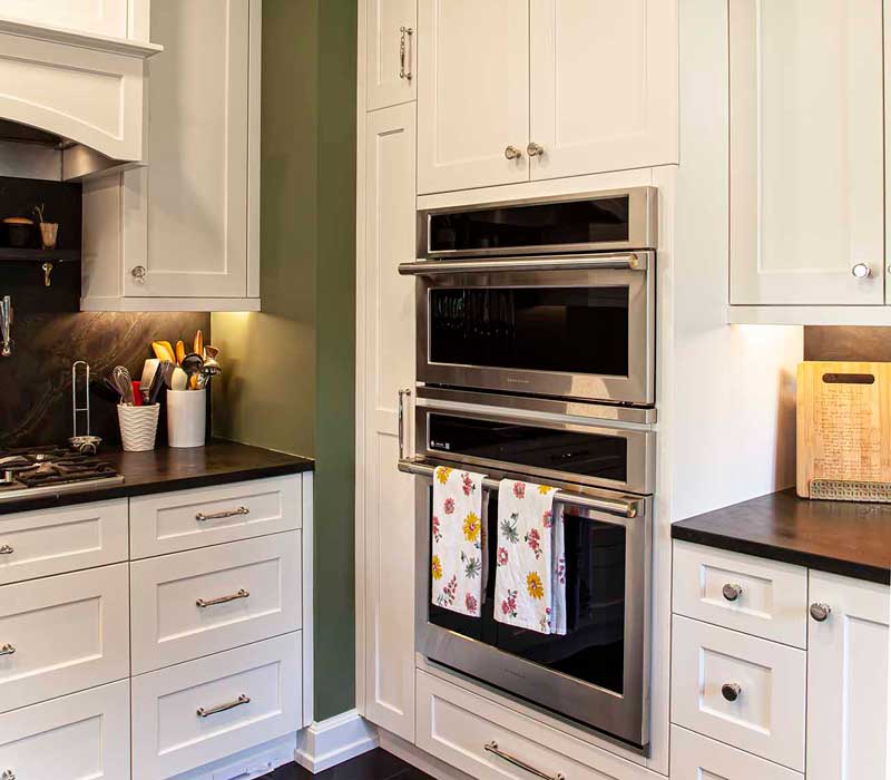 A chrome pull-down wheel faucet is the centerpiece of this traditional kitchen with natural slate countertops, art nouveau floral wallpaper, and green walls.