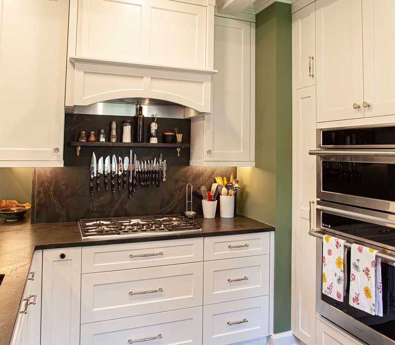 A chrome pull-down wheel faucet is the centerpiece of this traditional kitchen with natural slate countertops, art nouveau floral wallpaper, and green walls.