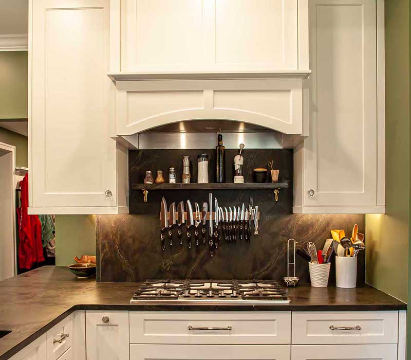 A chrome pull-down wheel faucet is the centerpiece of this traditional kitchen with natural slate countertops, art nouveau floral wallpaper, and green walls.