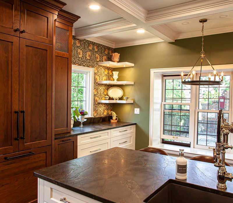 A chrome pull-down wheel faucet is the centerpiece of this traditional kitchen with natural slate countertops, art nouveau floral wallpaper, and green walls.