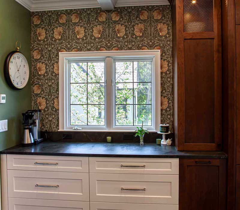 A chrome pull-down wheel faucet is the centerpiece of this traditional kitchen with natural slate countertops, art nouveau floral wallpaper, and green walls.